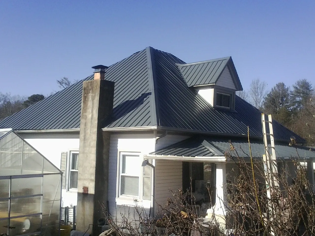 Dark blue standing seam metal roof on a white farmhouse with dormer — Slate & Tile Roof Repair by Roofing Brothers in Loris