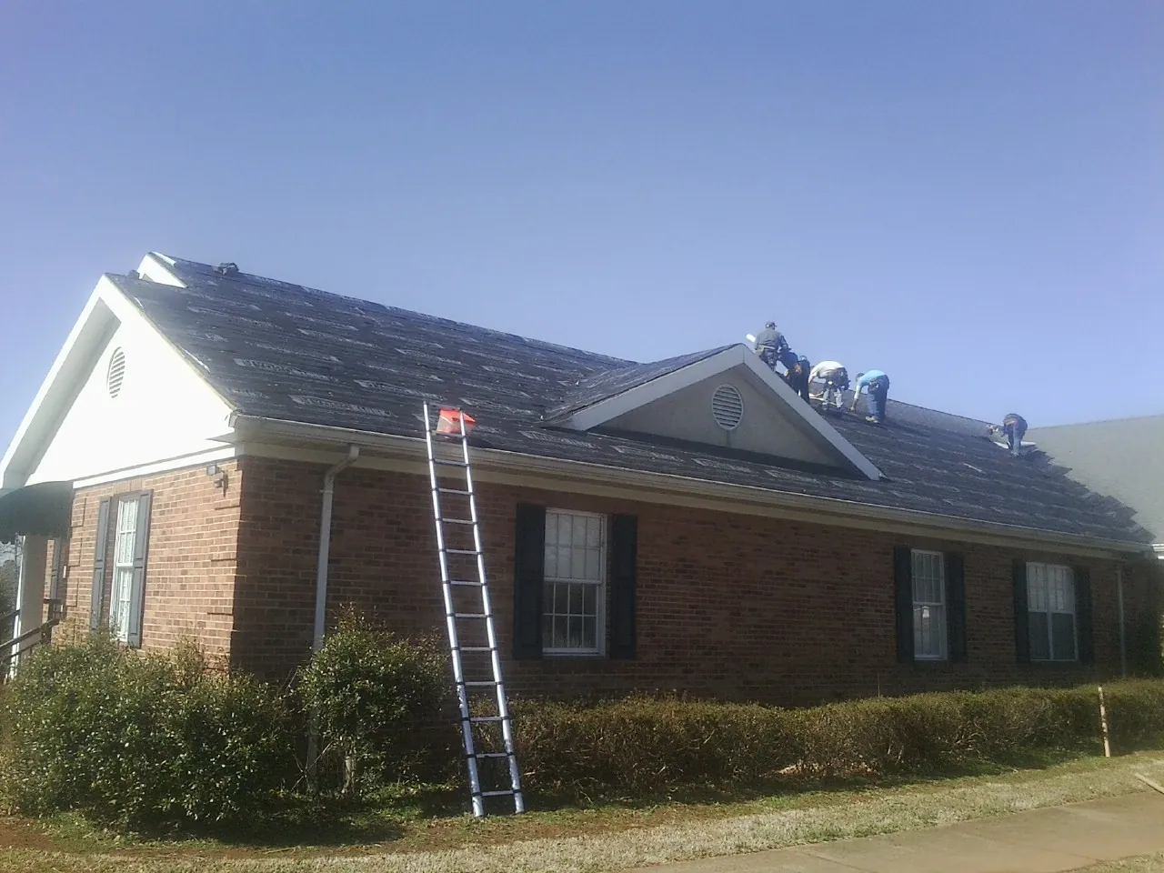 Crew tearing shingles off a brick ranch roof with a ladder set — Emergency Roof Repair work by our crew in Loris