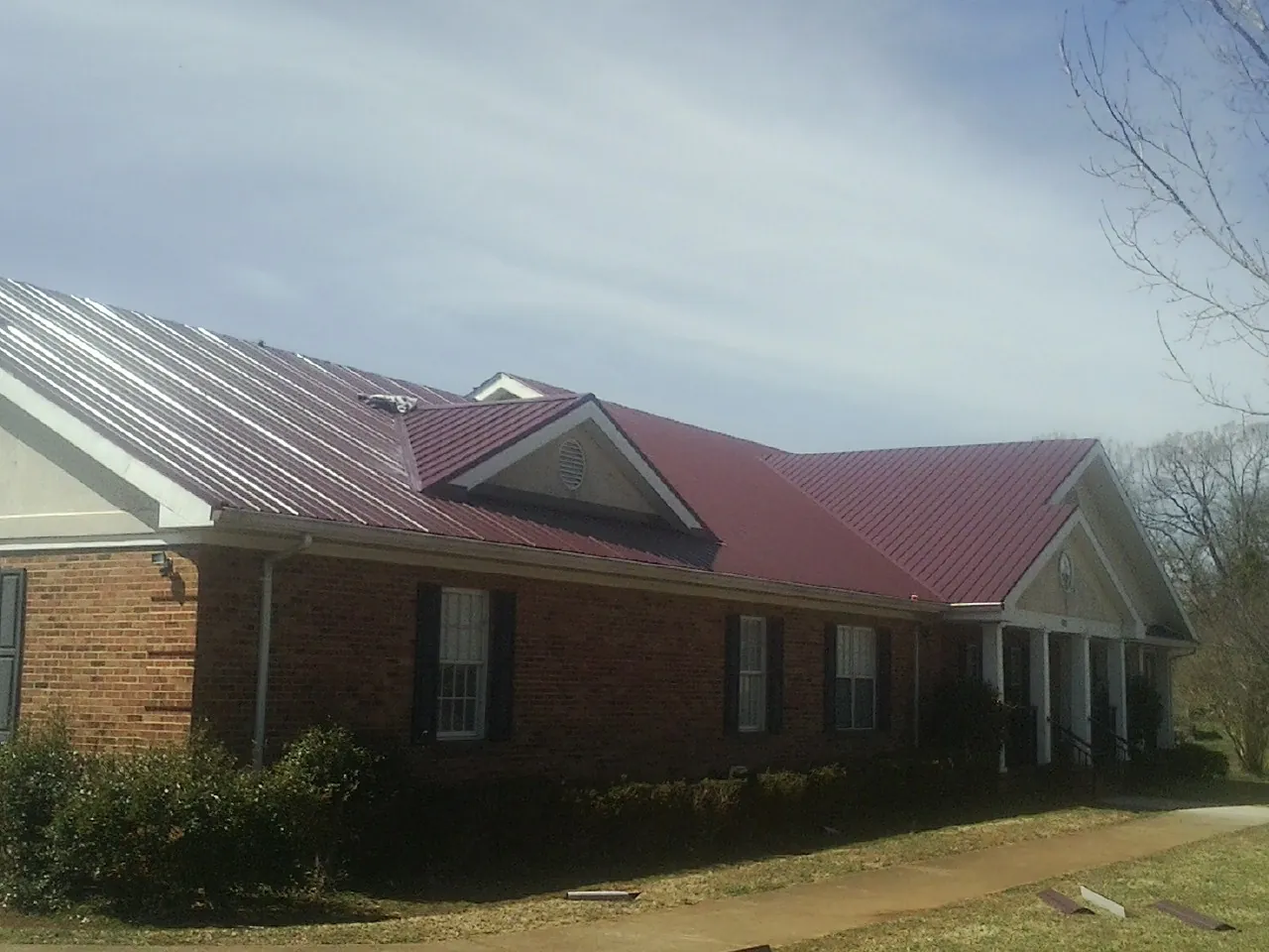 Red metal roof with gabled entries on a long brick building, from a Hail Damage Roof Repair job in Loris