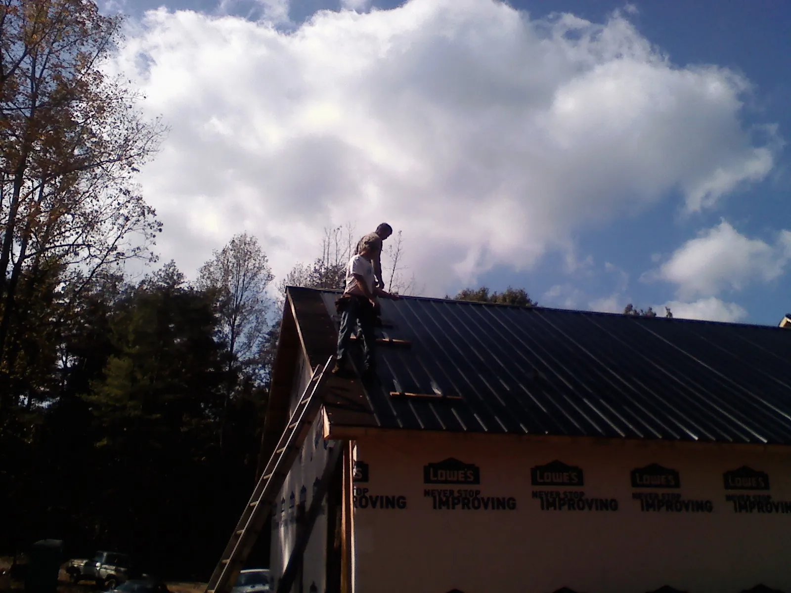 Roofer fastening dark metal panels high against a cloudy sky, from a Roof Inspection job in Loris