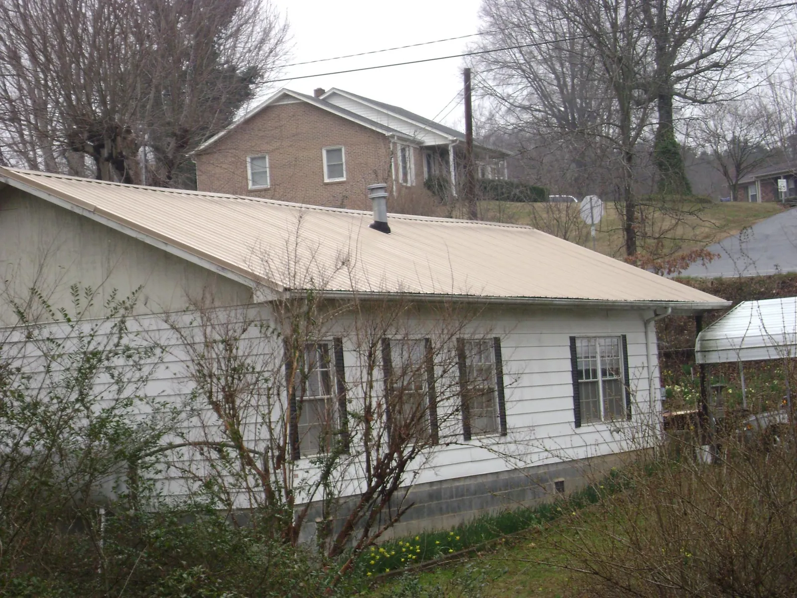Tan metal roof on a white sided house set into a hillside — Commercial Roofing by Roofing Brothers in Loris